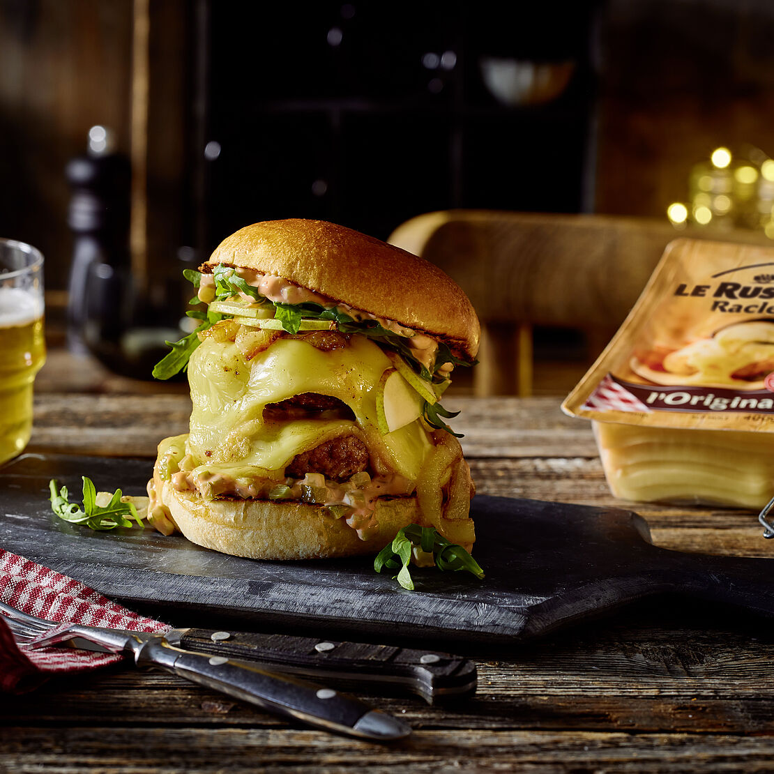 Großer Burger mit Raclette-Käse in einem Brioche-Brötchen serviert auf einer Schieferplatte