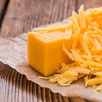 Großes Stück Cheddar Käse, teils gerieben in einem Papier auf einem Holztisch