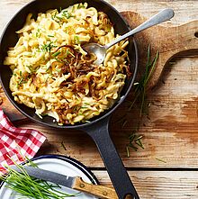 Käsespätzle Rezept mit MILKANA und Schmelzzwiebeln in der Pfanne auf einem Holzbrett serviert