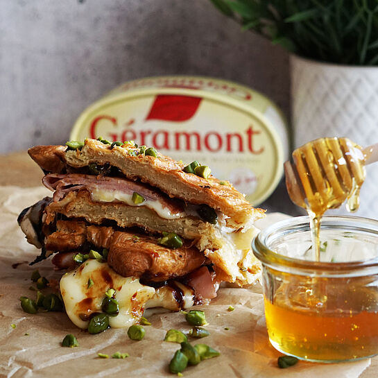 Knusprig geröstetes Croissant-Sandwich mit Géramont, Prosciutto, Honig, Balsamico-Creme und gehackten Pistazien.