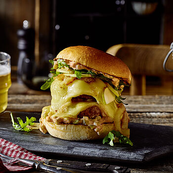 Großer Burger mit Raclette-Käse in einem Brioche-Brötchen serviert auf einer Schieferplatte