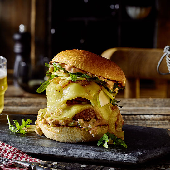 Großer Burger mit Raclette-Käse in einem Brioche-Brötchen serviert auf einer Schieferplatte